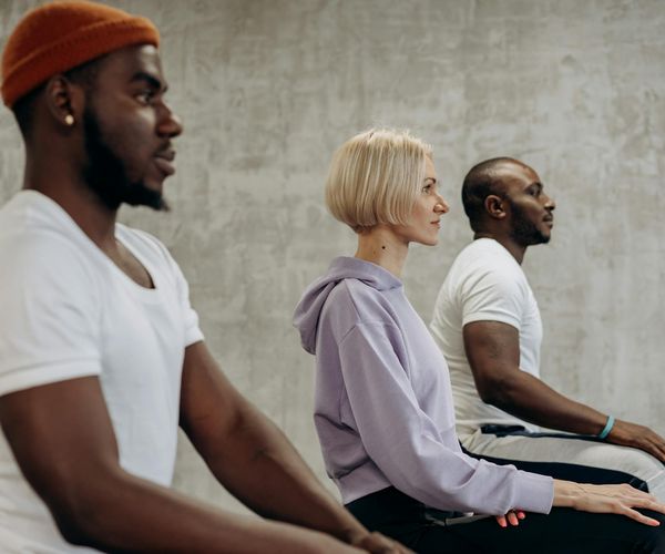 Diverse group of people sitting calmly in a bright, modern yoga studio.